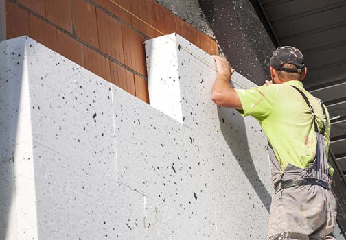 Arbeiter, der mit einer Kelle Mörtel auf die Styroporisolierung und das Netz aufträgt